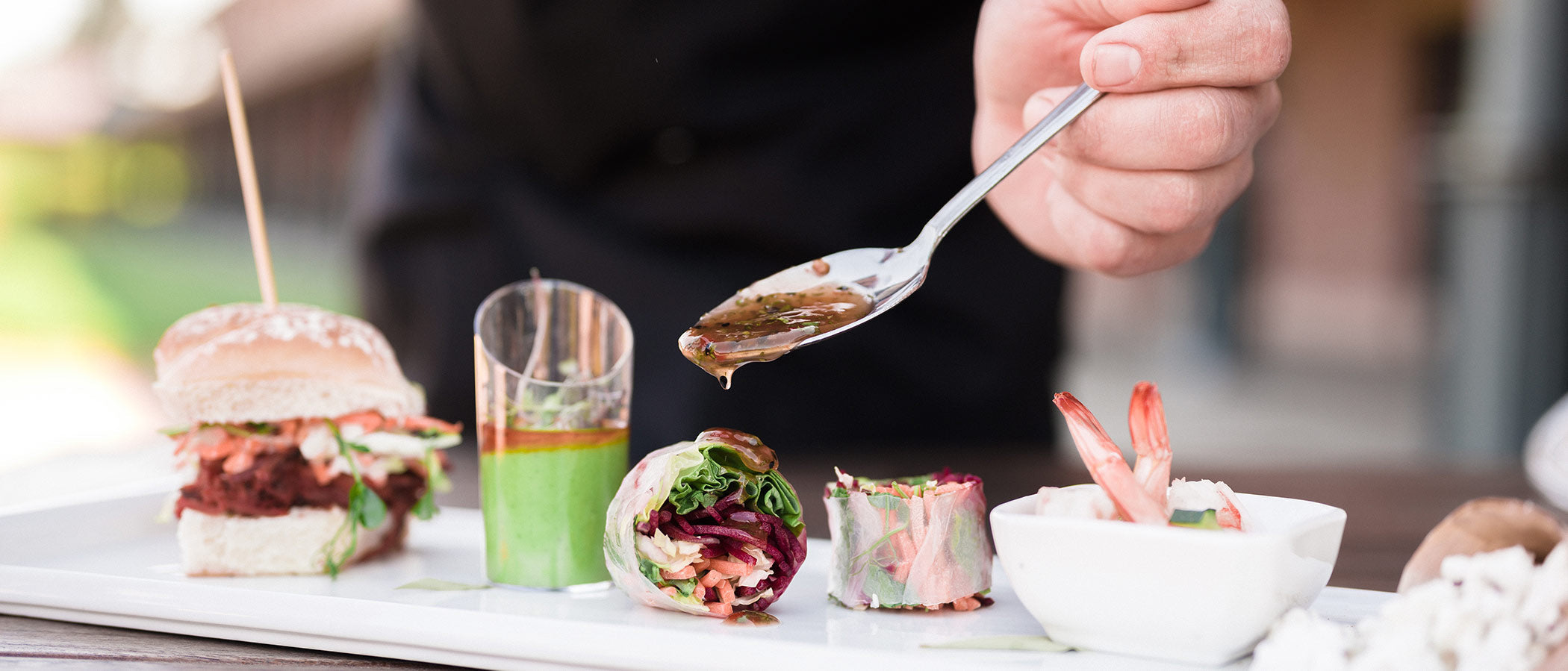 Chef is spooning sauce over a spring roll.