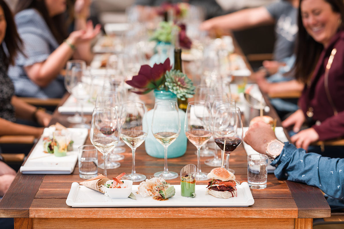 Food and wine on a table surrounded by people