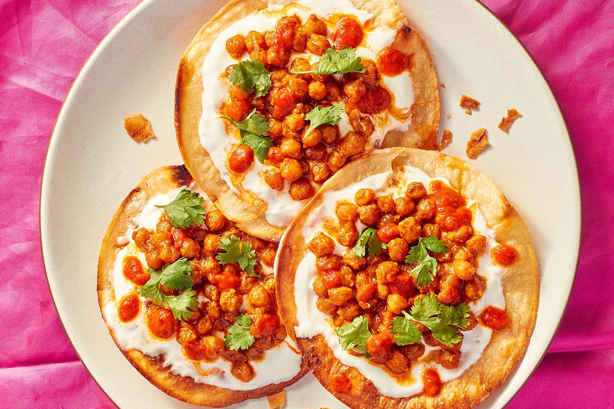 Three tostadas on a white plate and pink table cloth