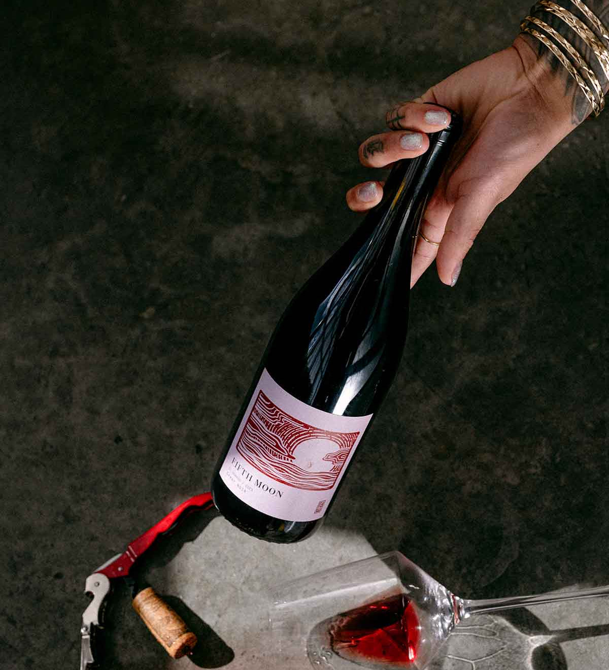 Hand reaching for a Fifth Moon wine bottle