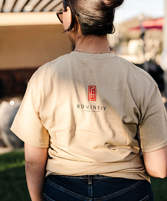 Close up of the back of a woman in khaki colored logo t-shirt