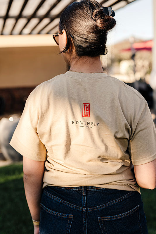 Close up of the back of a woman in khaki colored logo t-shirt