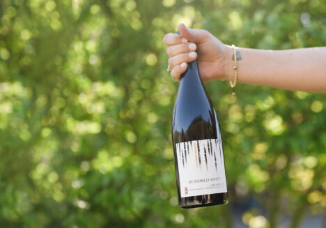 Hand holding RD Winery Hundred Knot Grenache in front of bushes.