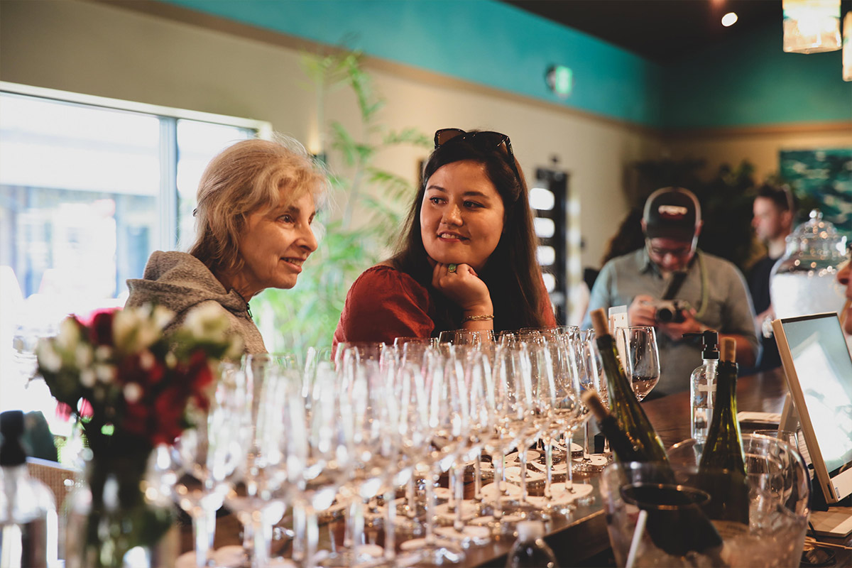 Woman smiling at another woman over rows of empty wine glasses
