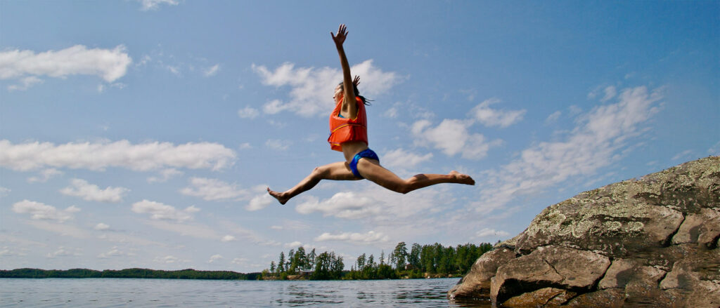 Woman jumping into lake with an orange life vest on.