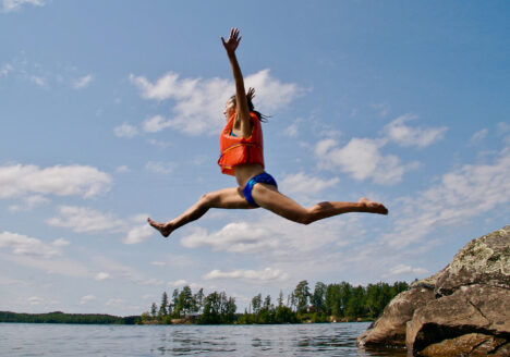 Woman jumping into lake with an orange life vest on.