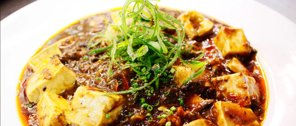 Vibrantly colored bowl of mapo tofu with thinly sliced green onions on top