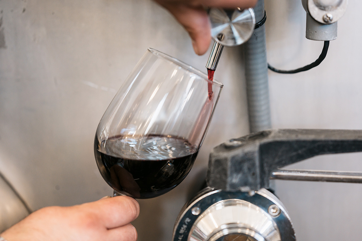 Hands operating a tank valve to fill glass with red wine.