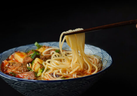 Close up of hand using chopsticks to pull ramen noodles from bowl