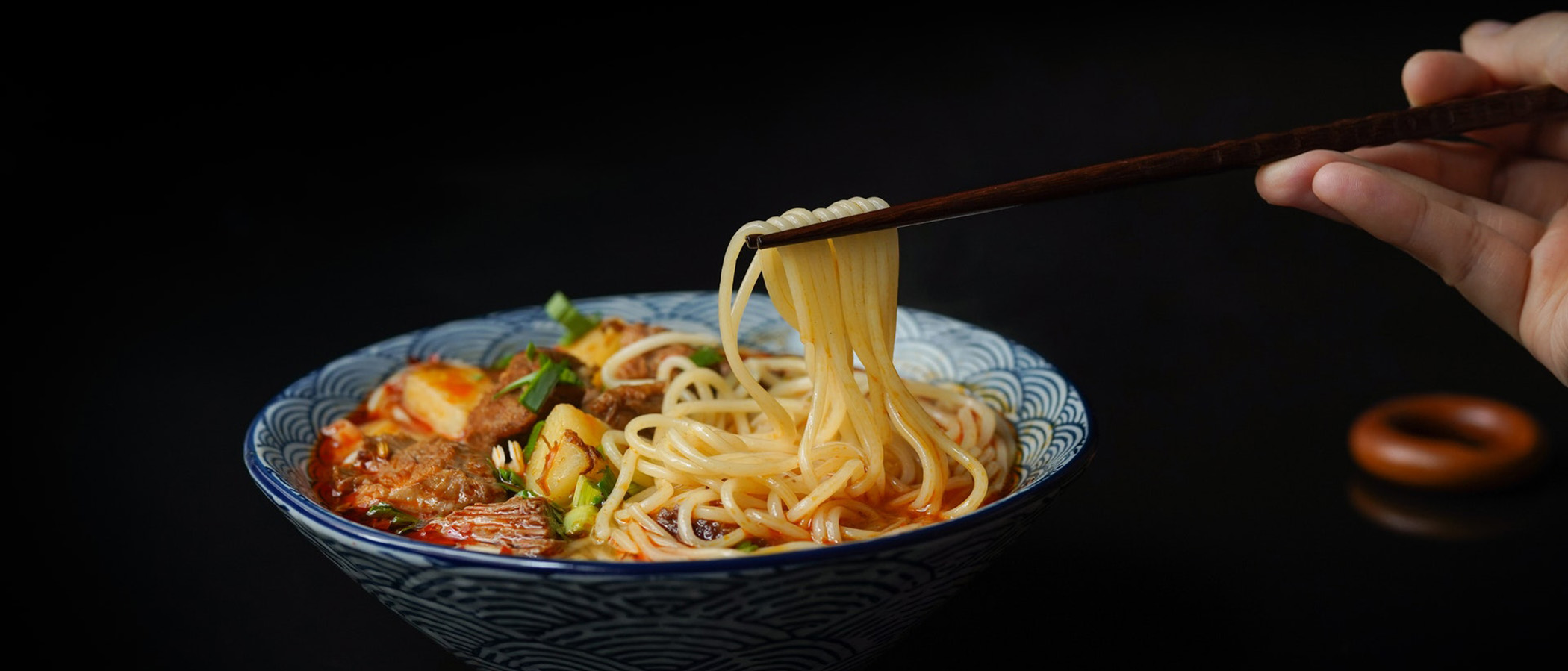 Close up of hand using chopsticks to pull ramen noodles from bowl