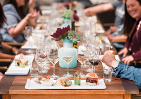 Food and wine on a table surrounded by people