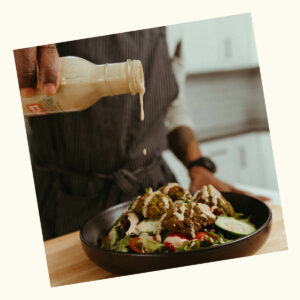 Hand pouring Plant Bomb Garlic Tahini sauce on falafel salad.