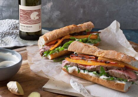 A table with two banh mi sandwiches, ginger pieces, and a bottle of white wine