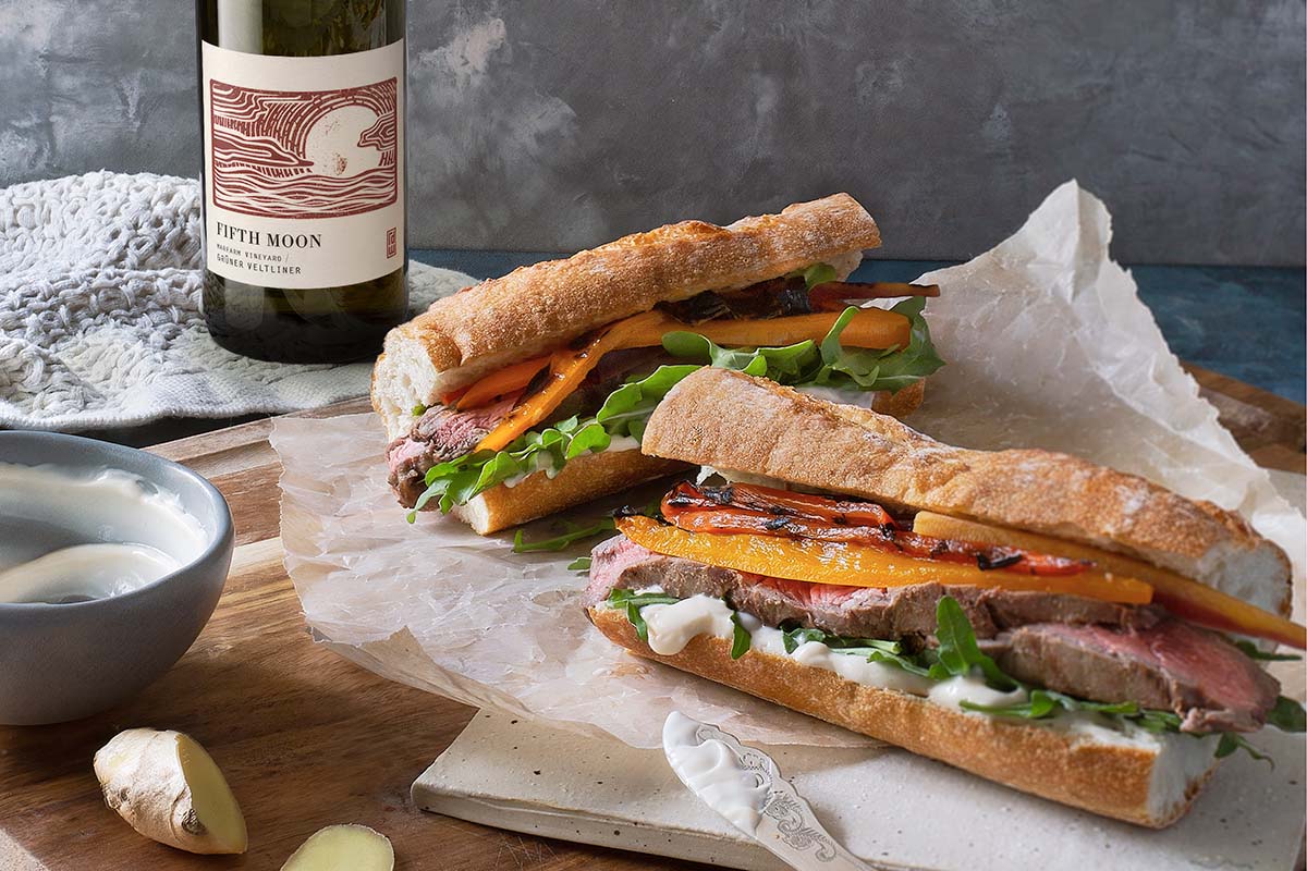 A table with two banh mi sandwiches, ginger pieces, and a bottle of white wine