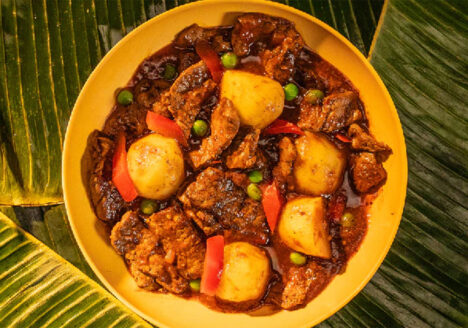 Yellow bowl of caldereta on banana leaves