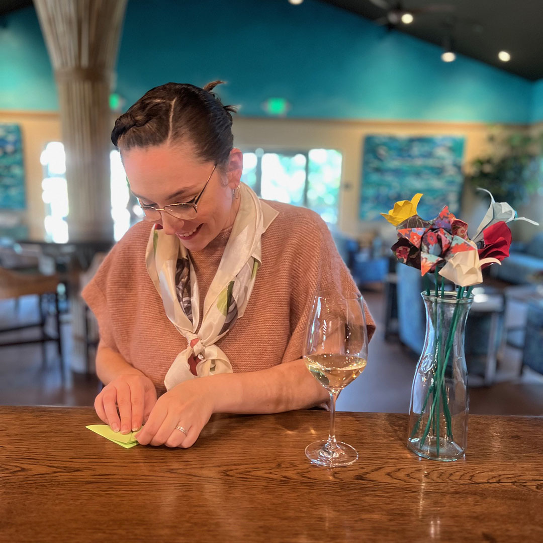 Woman at the bar with a glass of wine folding origami flowers