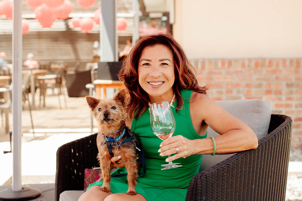 Woman in green dress with dog on lap and wine glass in hand