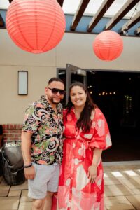 Woman in red dress and man in sunglasses smiling at camera under red lanterns