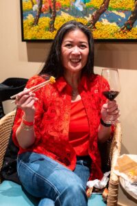 Woman in red sitting with chopsticks and glass of red wine in hand