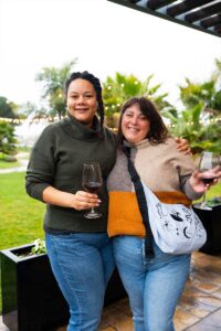 Two friends holding wine glasses posing for camera on outdoor patio